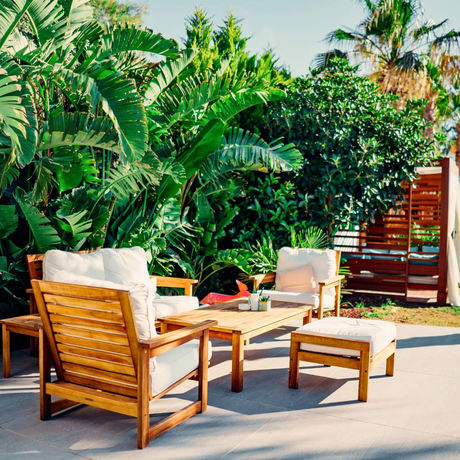 Lush tropical plants, including large palm trees and leafy shrubs, create a vibrant backdrop for a patio seating area.